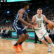 Action shot of a Boston Celtics player in a white home jersey dribbling past a Memphis Grizzlies defender in a blue away jersey at TD Garden.