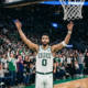Jayson Tatum of the Boston Celtics wearing a white #0 jersey, raising his arms in celebration on the basketball court during a home game at TD Garden.
