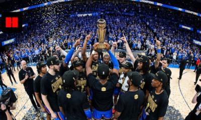 Wide-angle fisheye shot of the Oklahoma City Thunder players celebrating on a podium, holding the gold Larry O'Brien NBA Championship trophy amidst blue and gold confetti.