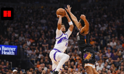 Basketball player taking a jump shot while defender contests the shot during a live game