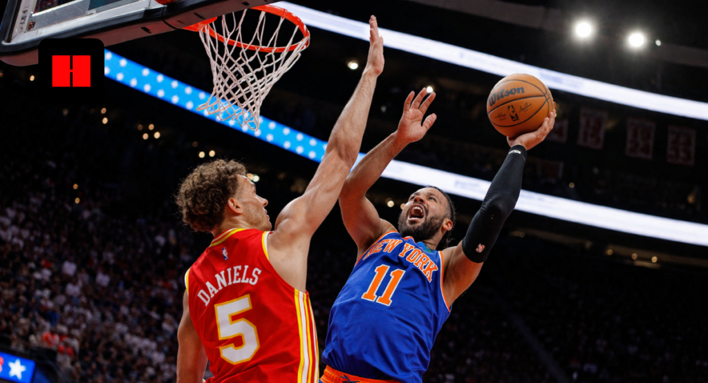 Low angle shot of a New York Knicks player attempting a layup while an Atlanta Hawks defender tries to block the shot during an NBA game in a packed arena
