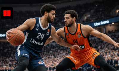 Professional basketball players in intense one-on-one dribble and defense matchup inside a packed arena with crowd and bright lights in UHD quality