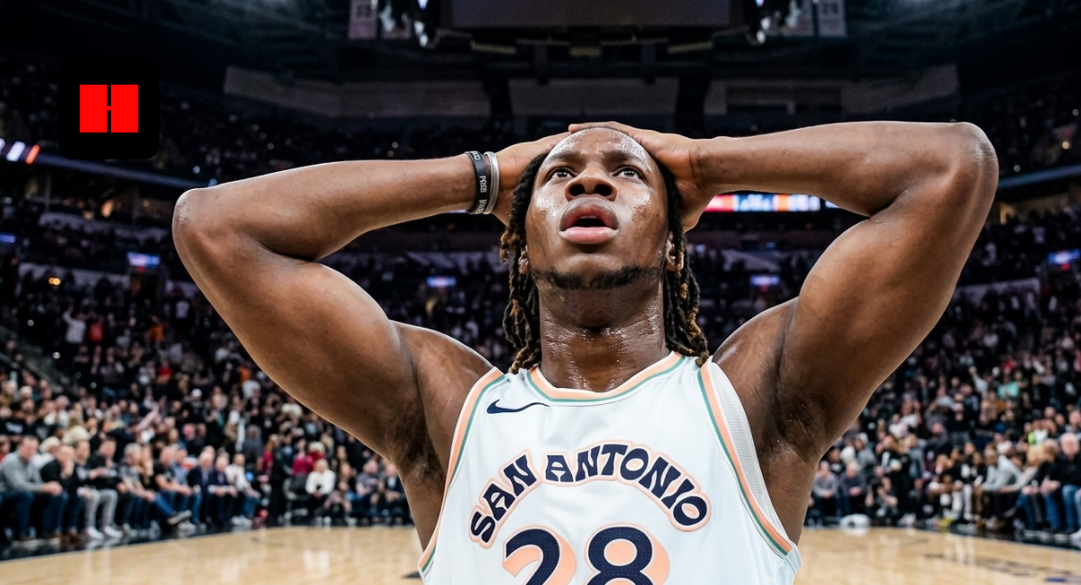 A low-angle shot of San Antonio Spurs player Charles Bassey (number 28) with his hands on his head in a crowded basketball arena.