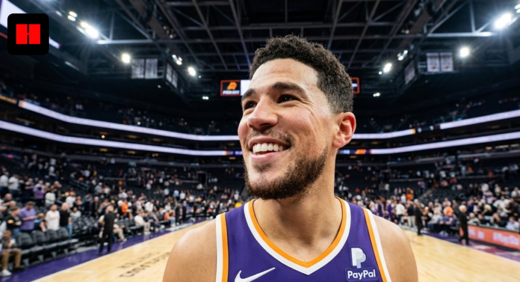 A wide-angle portrait of a smiling Devin Booker in his Phoenix Suns jersey on the basketball court, looking up at the scoreboard at Footprint Center.