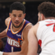 Devin Booker of the Phoenix Suns drives past a Toronto Raptors defender during an NBA game, showcasing ball control and offensive pressure in UHD action shot.