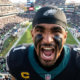 High-angle shot of Jalen Hurts yelling intensely at the camera in a crowded Eagles stadium.