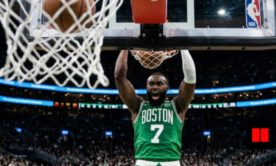 Jaylen Brown of the Boston Celtics screaming after a powerful two-handed dunk in a crowded NBA arena, viewed from under the basket.