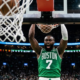 Jaylen Brown of the Boston Celtics screaming after a powerful two-handed dunk in a crowded NBA arena, viewed from under the basket.