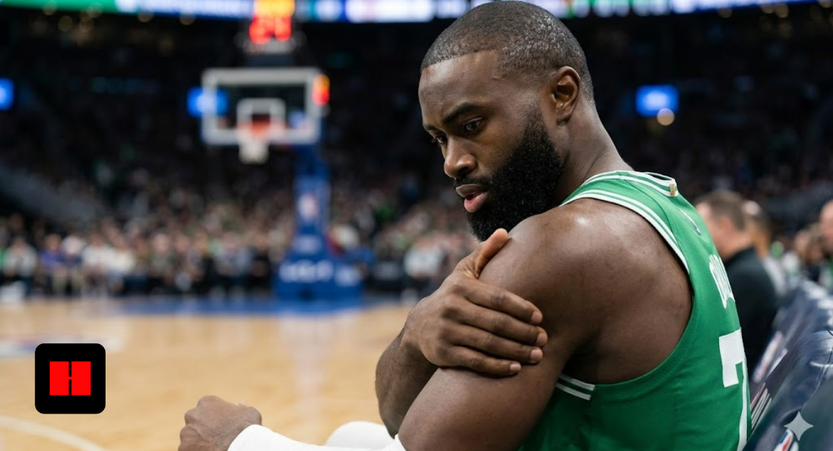 Jaylen Brown of the Boston Celtics sits on the bench holding his arm with a painful expression during an NBA game.