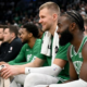 Boston Celtics stars Jaylen Brown and Kristaps Porzingis smiling and laughing while sitting on the team bench during an NBA game.