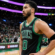Jayson Tatum standing on the court in a black and green Boston Celtics Statement Edition jersey with hands on hips.