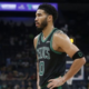 Boston Celtics forward Jayson Tatum in a black and green jersey standing on the basketball court with hands on hips during a game.
