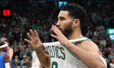 Jayson Tatum of the Boston Celtics holding his white jersey out in celebration during an NBA game, captured from a side angle with a blurred crowd in the background.