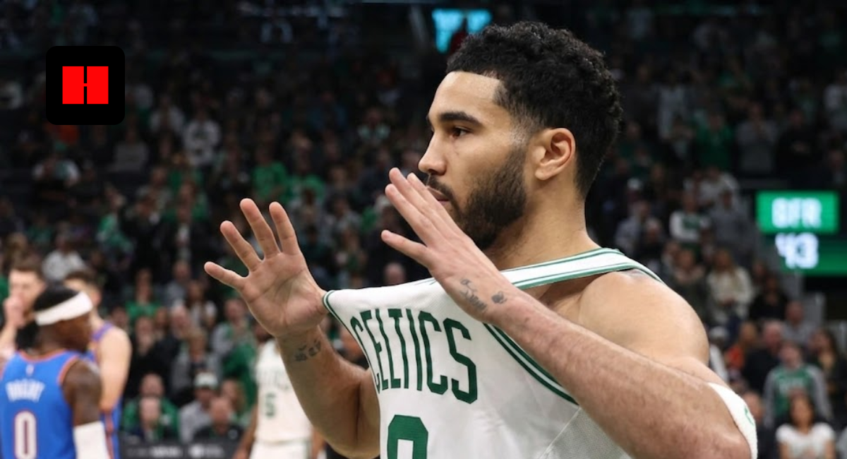 Jayson Tatum of the Boston Celtics holding his white jersey out in celebration during an NBA game, captured from a side angle with a blurred crowd in the background.
