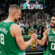 Jayson Tatum and Kristaps Porzingis shaking hands on the court in Boston Celtics green jerseys.