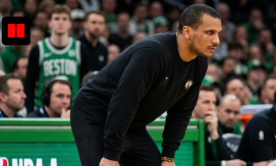 Boston Celtics head coach Joe Mazzulla leaning forward intensely on the sidelines during an NBA game, wearing a black crewneck sweatshirt with a small cross detail.