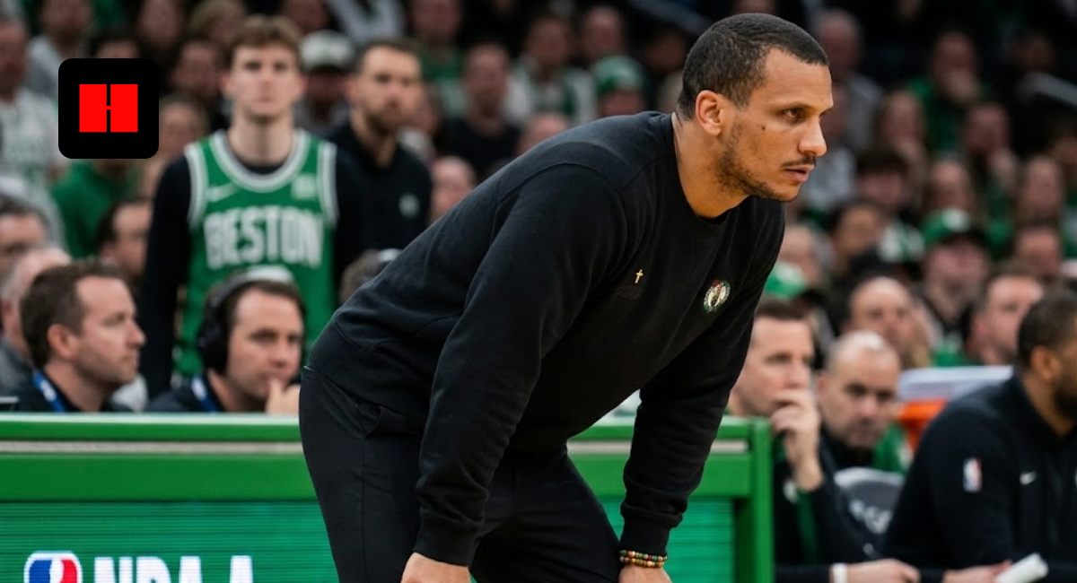 Boston Celtics head coach Joe Mazzulla leaning forward intensely on the sidelines during an NBA game, wearing a black crewneck sweatshirt with a small cross detail.