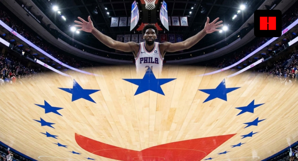 Joel Embiid with arms outstretched over a stylized Philadelphia 76ers court with blue stars inside a packed NBA arena
