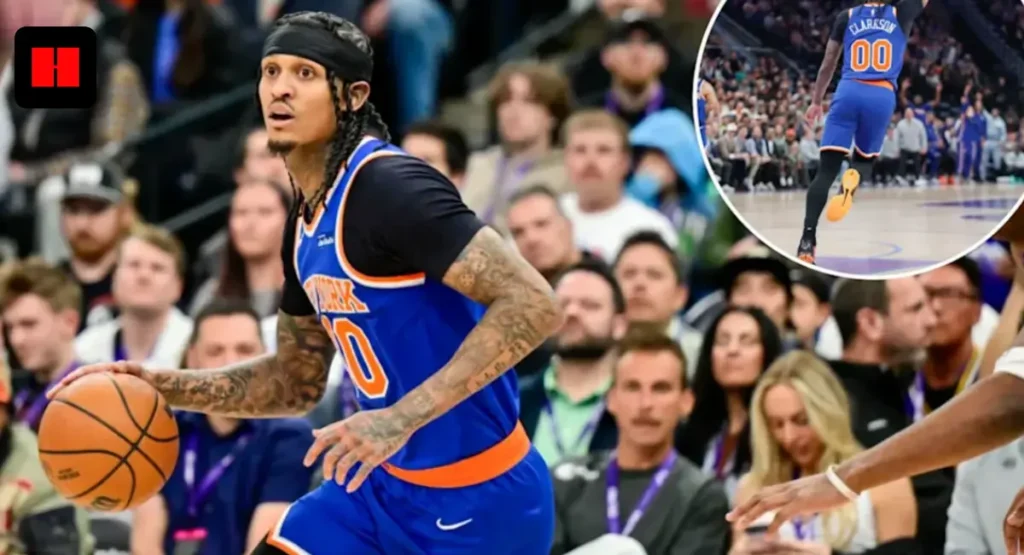 NBA player Jordan Clarkson in a blue New York Knicks uniform with number 00, shooting a jump shot during a game with a crowded arena in the background.