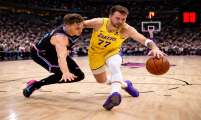 Luka Doncic of the Los Angeles Lakers drives past a Miami Heat defender during an NBA game, captured from a low-angle courtside view with the crowd in the background.