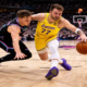Luka Doncic of the Los Angeles Lakers drives past a Miami Heat defender during an NBA game, captured from a low-angle courtside view with the crowd in the background.