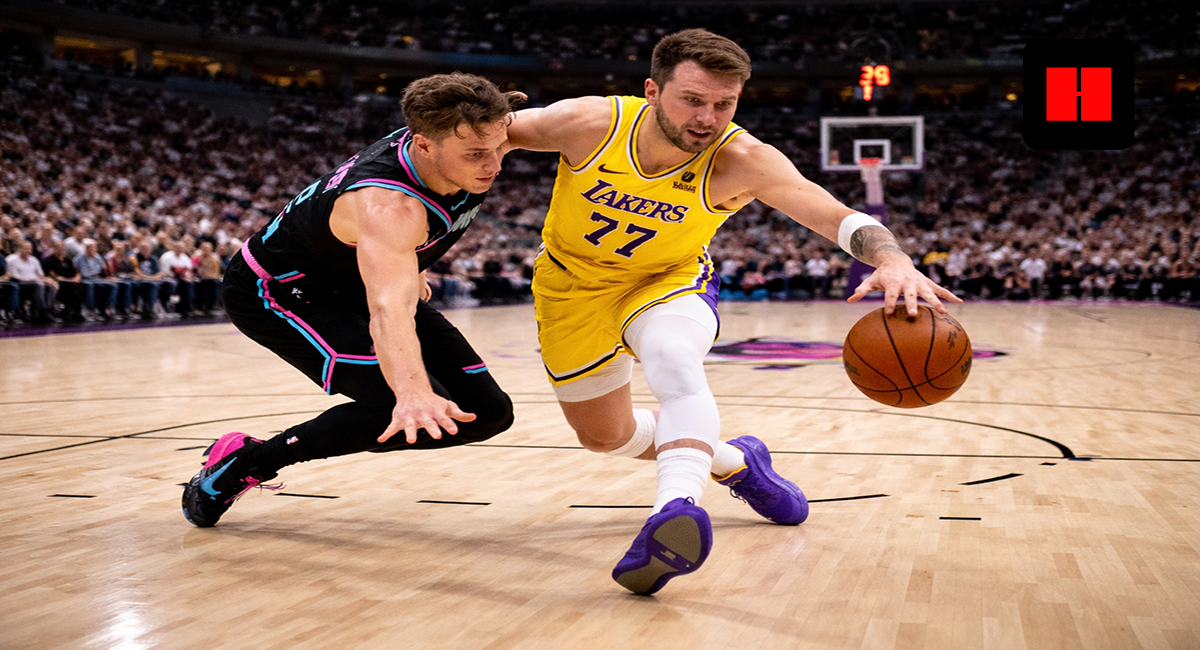 Luka Doncic of the Los Angeles Lakers drives past a Miami Heat defender during an NBA game, captured from a low-angle courtside view with the crowd in the background.