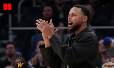 NBA player standing courtside and clapping while encouraging teammates during a professional basketball game with crowd in the background