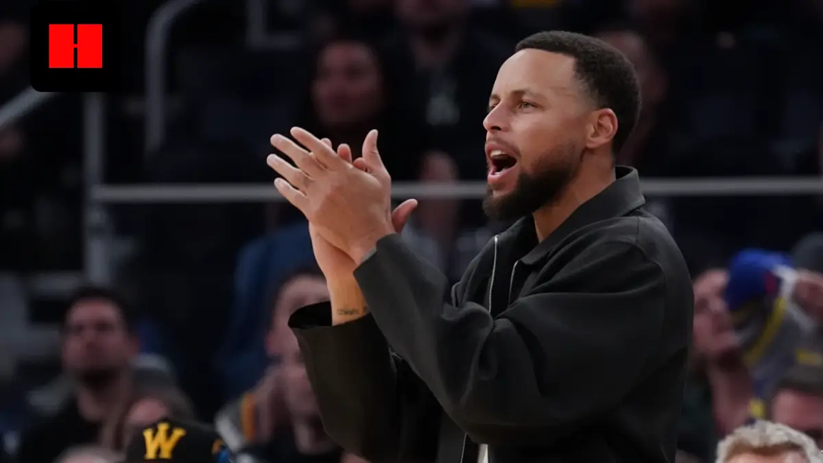 NBA player standing courtside and clapping while encouraging teammates during a professional basketball game with crowd in the background