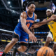 A low-angle, wide-lens action shot of New York Knicks forward OG Anunoby (number 8) dribbling a Wilson basketball past Indiana Pacers forward Jarace Walker (number 5) in a crowded NBA arena.