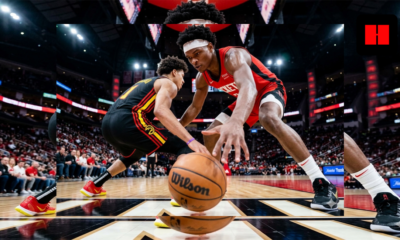 A Houston Rockets defender reaches for the ball while guarding an Atlanta Hawks player dribbling at the top of the key, captured from a low courtside angle during an NBA game.
