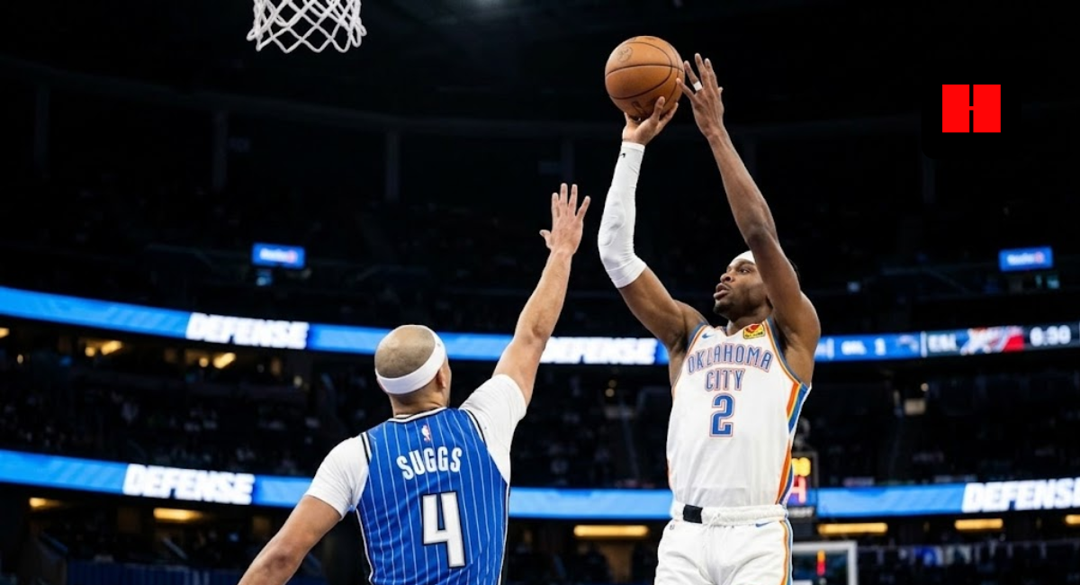 Oklahoma City Thunder player Shai Gilgeous-Alexander (2) takes a shot as Jalen Suggs (4) of the Orlando Magic tries to block it during an NBA game. The OKC player is in mid-air with the ball high above his head, wearing his white uniform, while the Magic player defends from behind.