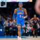 Shai Gilgeous-Alexander wearing a blue Oklahoma City Thunder jersey celebrating on the basketball court during an NBA game.