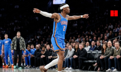Shai Gilgeous-Alexander of the Oklahoma City Thunder celebrating on the court with arms outstretched, wearing a blue jersey and white headband during an NBA game.