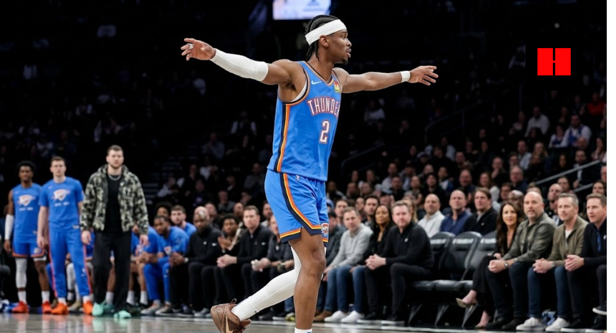 Shai Gilgeous-Alexander of the Oklahoma City Thunder celebrating on the court with arms outstretched, wearing a blue jersey and white headband during an NBA game.