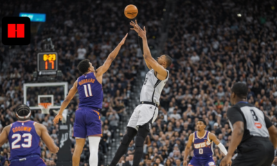 San Antonio Spurs player attempts jump shot over Phoenix Suns defender during intense NBA game action in crowded arena.