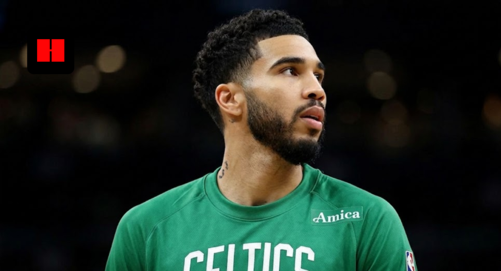 Jayson Tatum of the Boston Celtics looking up from the sidelines in a green team warmup shirt.