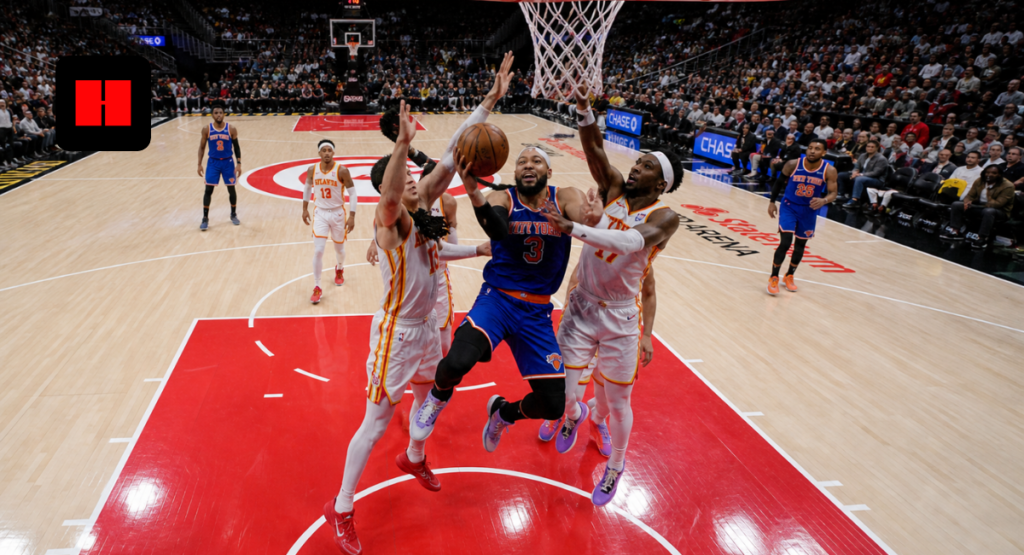 New York Knicks player attempting a contested layup against Atlanta Hawks defenders during an NBA game in a packed arena.